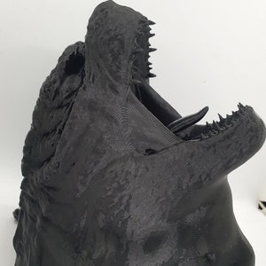 May include: A black 3D printed model of a dragon's head with an open mouth and sharp teeth.