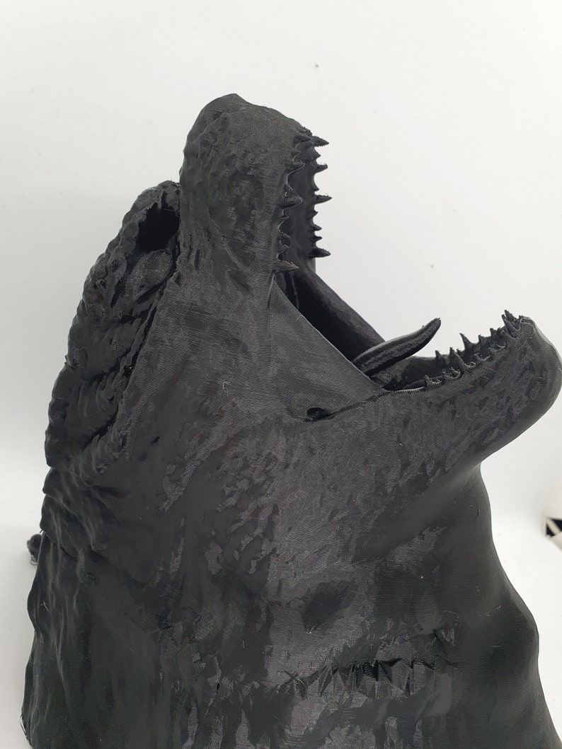 May include: A black 3D printed model of a dragon's head with an open mouth and sharp teeth.