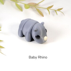 May include: A small, gray, clay sculpture of a baby rhinoceros. The rhino has a small, white horn and black eyes.