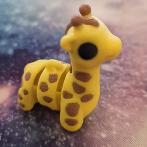May include: A small yellow and brown giraffe figurine with a segmented body. The giraffe has a large black eye and a brown nose.