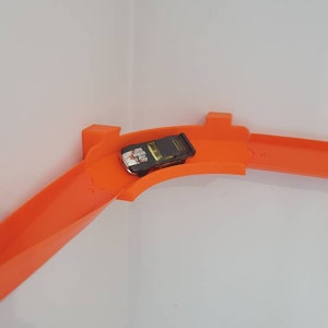 May include: Orange plastic track for toy cars, with a black toy car on the track.