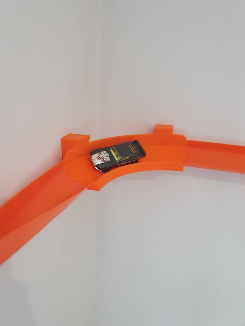 May include: Orange plastic track for toy cars, with a black toy car on the track.