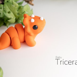 TriceraTwirl™ Baby Triceratops Fidget Keyring: "A tiny, hand-crafted baby triceratops keychain with colorful details. The triceratops has a large frill, three small horns, and a round, chubby body.