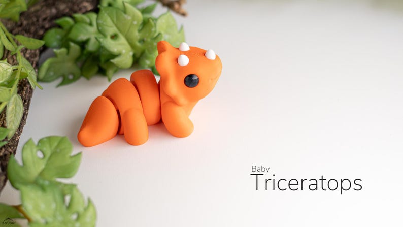 TriceraTwirl™ Baby Triceratops Fidget Keyring: "A tiny, hand-crafted baby triceratops keychain with colorful details. The triceratops has a large frill, three small horns, and a round, chubby body.