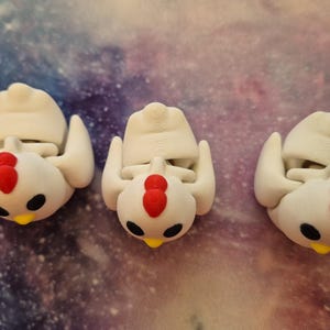 May include: Three white ceramic chicken figurines with red combs and black eyes. The chickens are in a standing position with their wings outstretched.