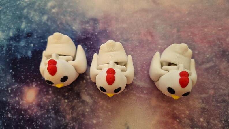 May include: Three white ceramic chicken figurines with red combs and black eyes. The chickens are in a standing position with their wings outstretched.