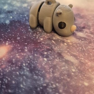 May include: A small, gray, 3D printed rhinoceros figurine. The figurine has a textured surface and a black eye.