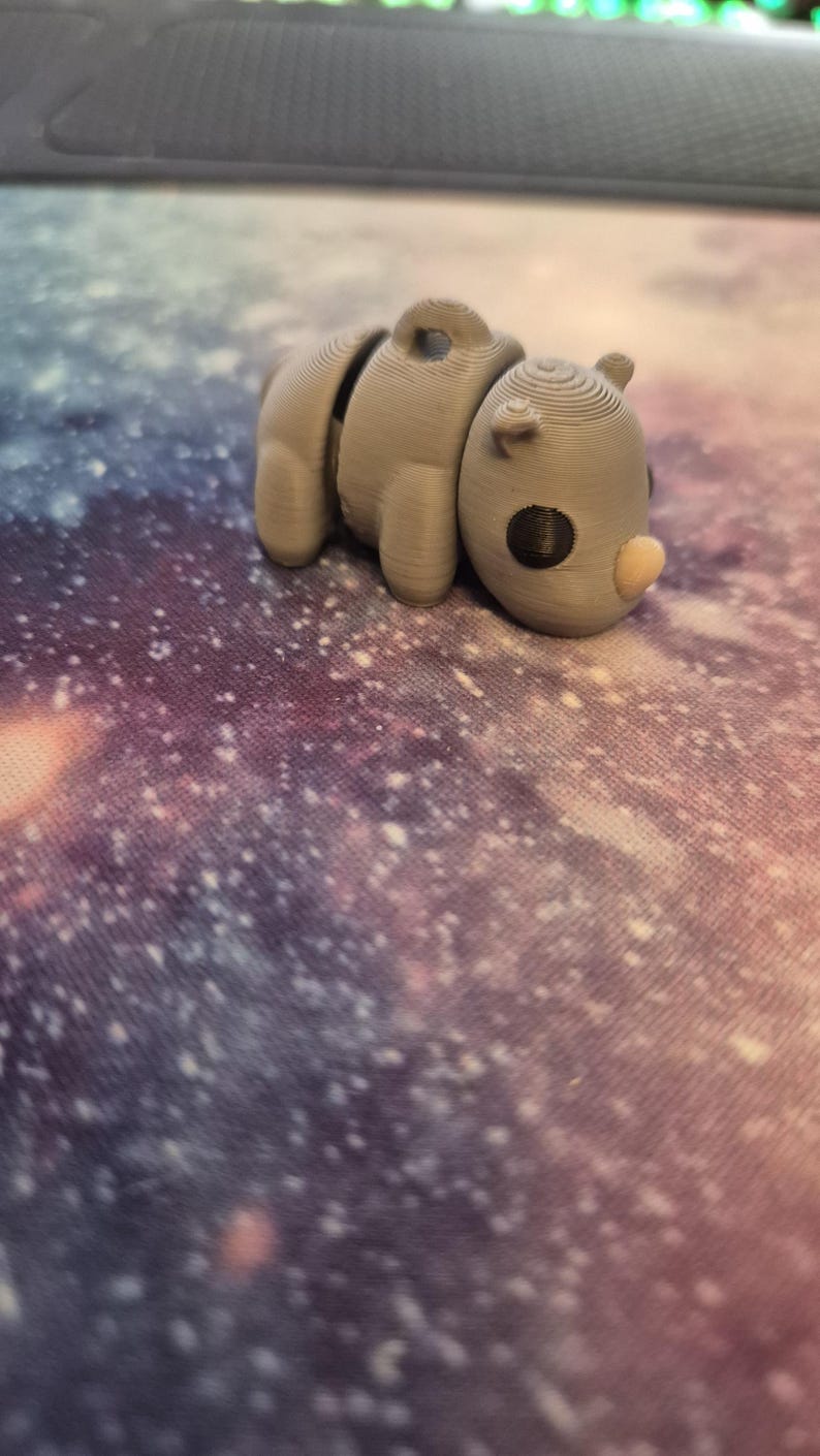 May include: A small, gray, 3D printed rhinoceros figurine. The figurine has a textured surface and a black eye.