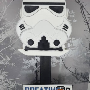 May include: A white 3D printed model of a Star Wars Stormtrooper helmet on a black stand. The stand has a yellow base with the text "CREATIVE 3D SOLUTIONS" on a white plaque.