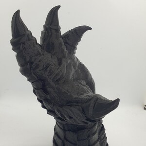 May include: A black 3D printed dragon claw sculpture with sharp, detailed claws and a textured wrist.