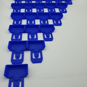 May include: Arrangement of blue plastic components, each with a rectangular tray and a U-shaped clip. The components are stacked in a descending order, creating a stepped pattern. The objects are on a white background.