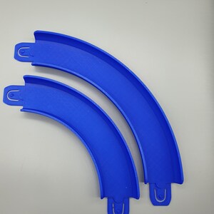 May include: Two blue plastic track pieces for a toy race car track. The pieces are curved and connect together.