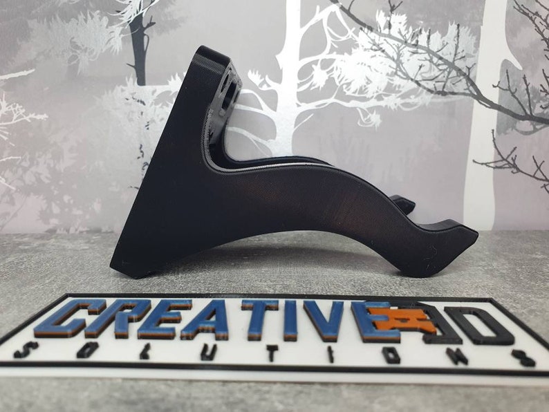 May include: A black plastic wall mount with a curved design. The mount is designed to hold a device, such as a phone or tablet, in a horizontal position.