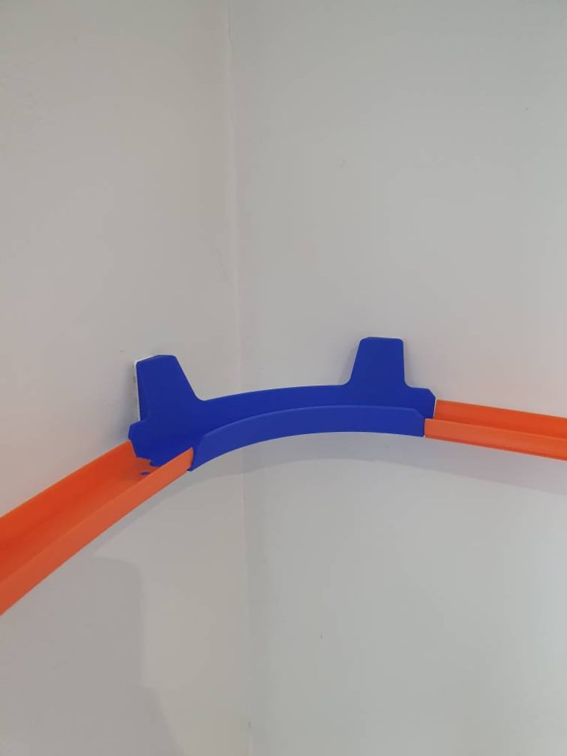 May include: A blue plastic track piece for a toy car race track. The track piece is designed to fit in a corner and has two orange track pieces attached to it.