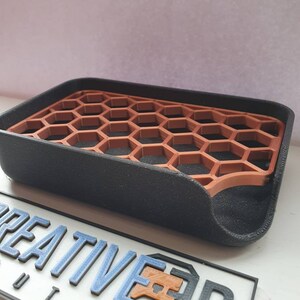May include: A black soap dish with a honeycomb design. The honeycomb is made of a brown plastic material. The dish has a curved edge and a slight lip around the edge.