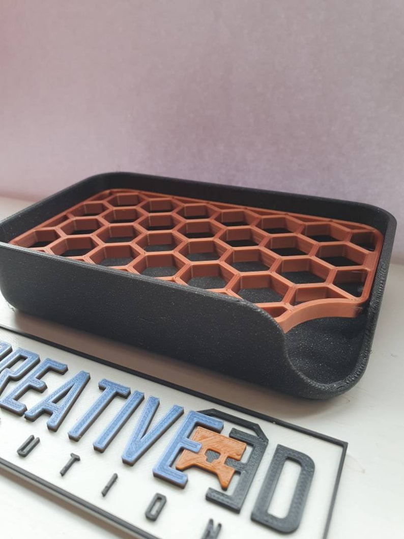 May include: A black soap dish with a honeycomb design. The honeycomb is made of a brown plastic material. The dish has a curved edge and a slight lip around the edge.