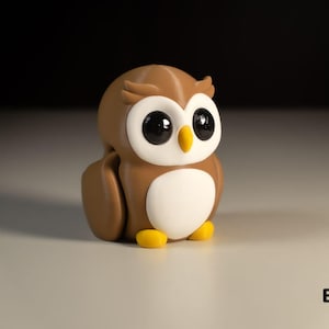 May include: A brown and white owl figurine with large eyes and yellow feet. The owl is sitting on a white surface. "Baby Owl" is written in black text below the owl.