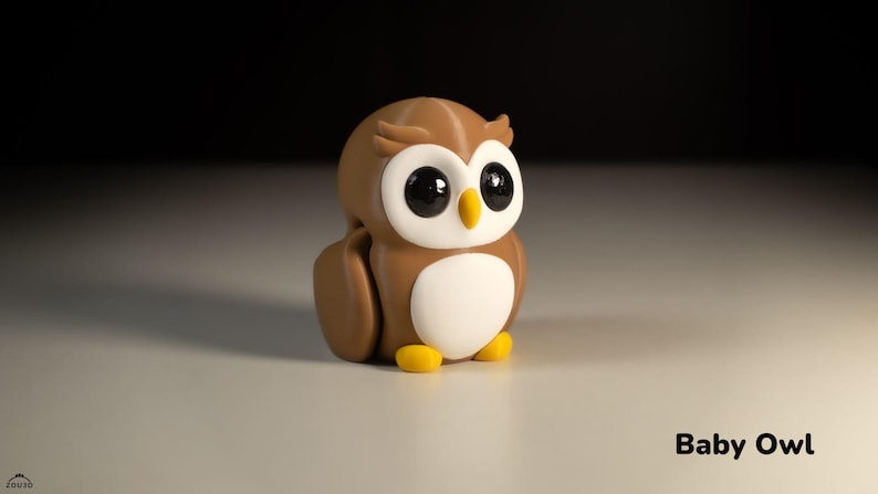 May include: A brown and white owl figurine with large eyes and yellow feet. The owl is sitting on a white surface. "Baby Owl" is written in black text below the owl.
