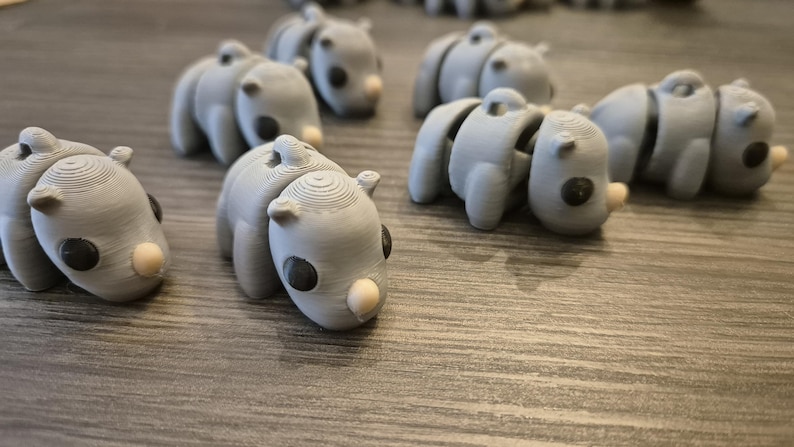 K&ouml;nnte beinhalten: Eine Sammlung von grauen, artikulierten, 3D-gedruckten Tierfiguren. Die Figuren haben die Form eines Nashorns mit einem runden K&ouml;rper und einem kleinen Horn auf der Nase. Die Figuren haben schwarze Augen und eine wei&szlig;e Nase.