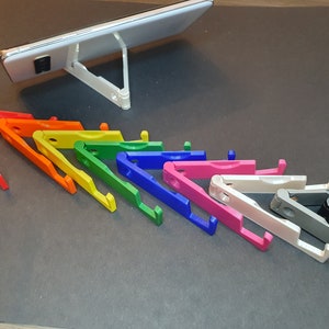 Puede incluir: Un conjunto de diez soportes para tel&eacute;fono de colores, dispuestos en forma de arco&iacute;ris. Los soportes est&aacute;n hechos de pl&aacute;stico y se pliegan en un tama&ntilde;o compacto. Est&aacute;n dise&ntilde;ados para sostener un tel&eacute;fono para una visualizaci&oacute;n con manos libres.