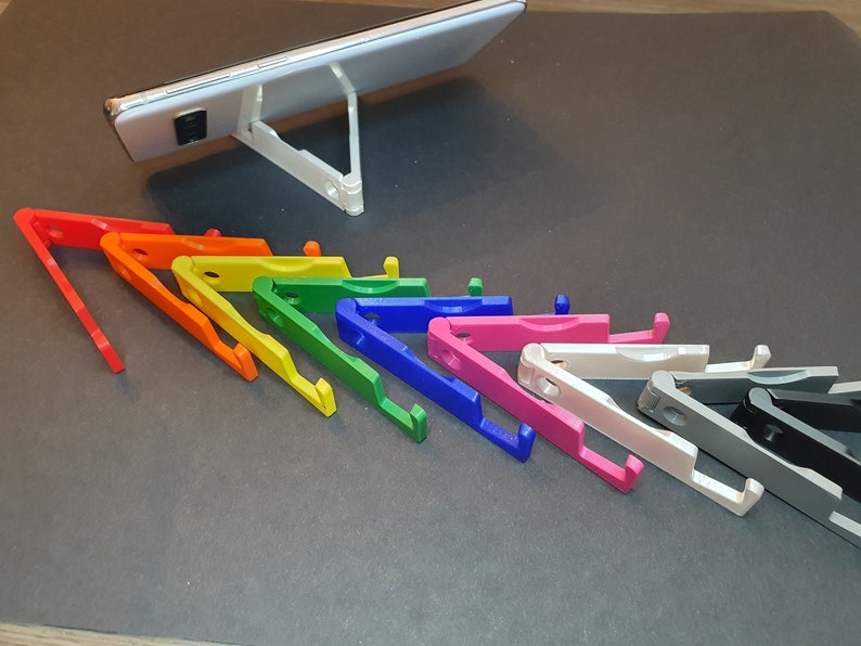 Puede incluir: Un conjunto de diez soportes para tel&eacute;fono de colores, dispuestos en forma de arco&iacute;ris. Los soportes est&aacute;n hechos de pl&aacute;stico y se pliegan en un tama&ntilde;o compacto. Est&aacute;n dise&ntilde;ados para sostener un tel&eacute;fono para una visualizaci&oacute;n con manos libres.