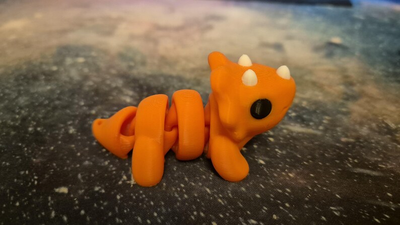 May include: Orange and white segmented toy dinosaur with a curled tail and three horns on its head.