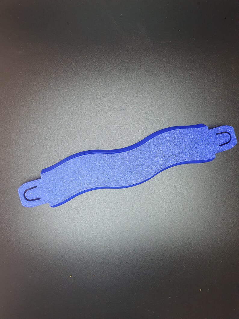 May include: A blue plastic track piece for a toy race car set. The piece is shaped like a curved S and has two small loops on either end.