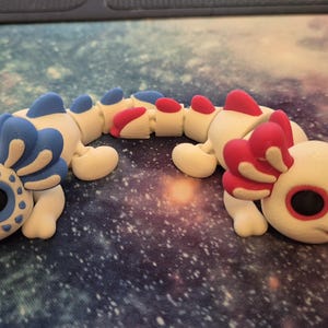 May include: Two white axolotl figurines with articulated bodies. One axolotl has blue and white gills and the other has pink and white gills.