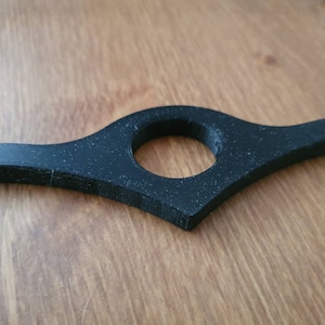 May include: A black plastic bookmark with a curved design and a hole in the center.
