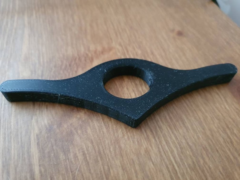 May include: A black plastic bookmark with a curved design and a hole in the center.