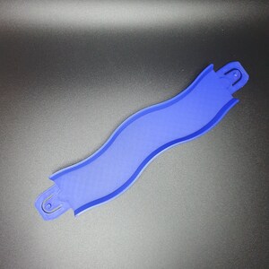 May include: A blue plastic track piece for a toy race car track. The piece is curved and has a textured surface.