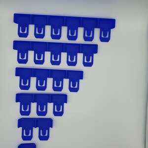 May include: A collection of blue plastic clips arranged in a descending staircase pattern. Each clip has a rectangular top with a U-shaped opening. The clips are a vibrant shade of blue and appear to be new.
