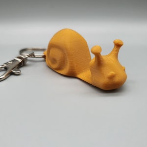 May include: A gold-colored snail keychain with a silver metal key ring.