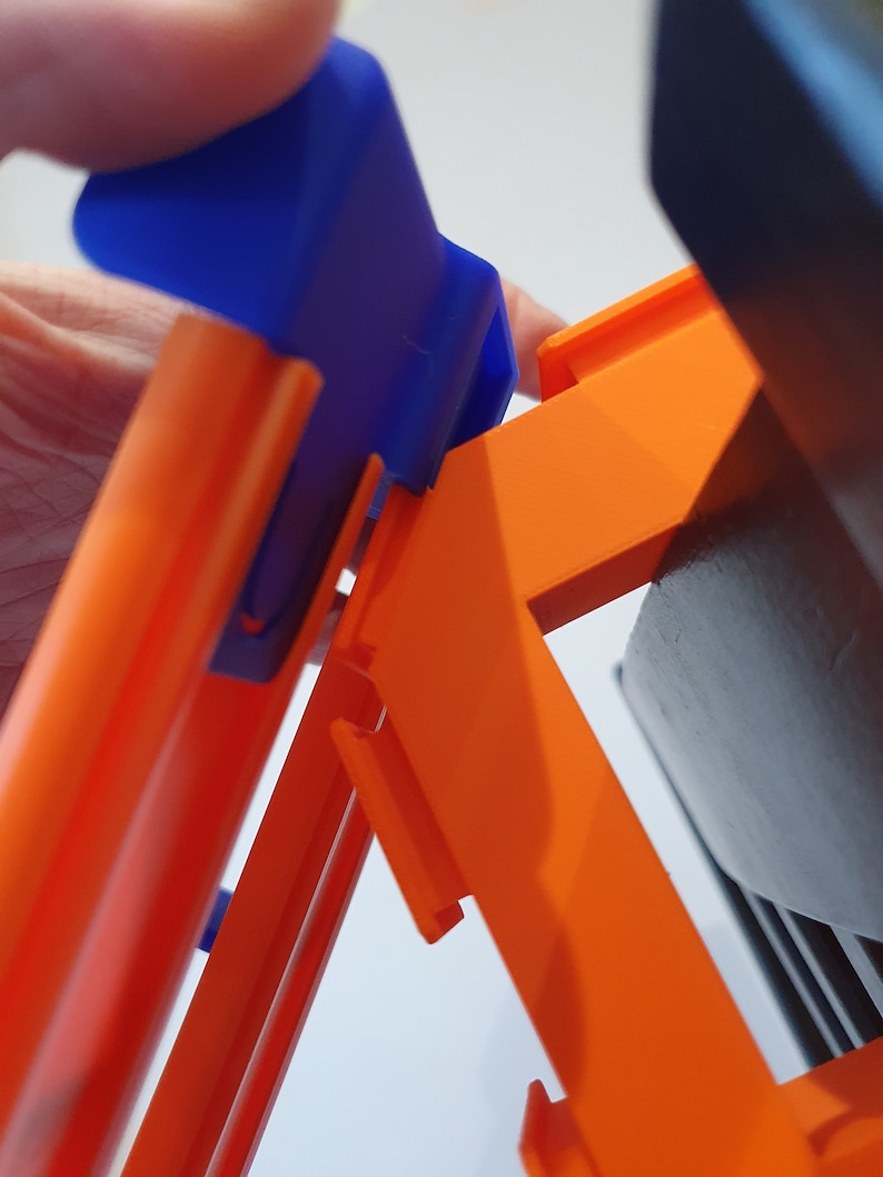 May include: A close-up of a blue and orange toy track set. The blue piece is a connector that fits into the orange track.