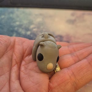 May include: A small gray 3D printed rhinoceros figurine with black eyes and a light brown nose.