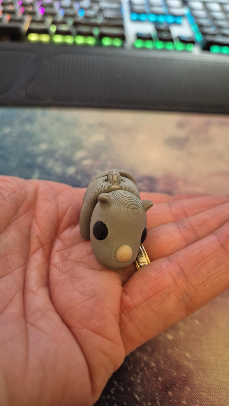 May include: A small gray 3D printed rhinoceros figurine with black eyes and a light brown nose.