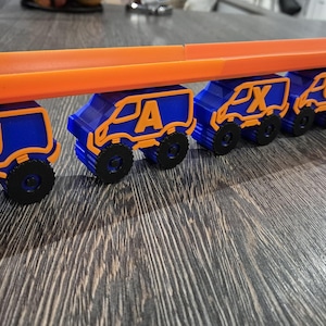 May include: A toy truck train with blue and orange cars. Each car has a letter on it, spelling out the name "JAXXON".
