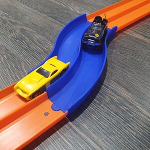 May include: A blue and orange plastic toy race track with two toy cars. One car is yellow and the other is black with the word "Police" on the side.