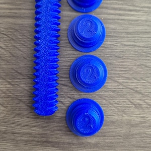 May include: Four blue plastic caps with the number "2" printed on them, and a blue plastic gear-shaped piece.