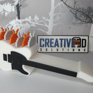 May include: A white 3D printed electric guitar with a black pickguard and a row of orange and gray pixelated figures on top. The guitar is lying on a white surface. The text "CREATIVE 3D SOLUTIONS" is visible in the background.
