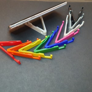Puede incluir: Un conjunto de soportes para tel&eacute;fono de colores, dispuestos en forma de arco&iacute;ris, con un soporte para tel&eacute;fono blanco y un soporte para tel&eacute;fono negro en el fondo.