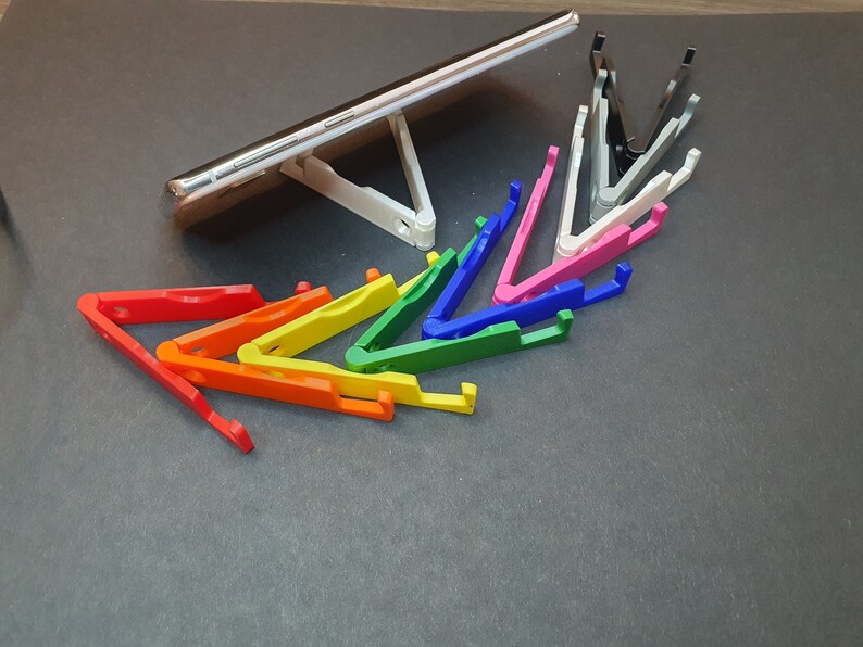 Puede incluir: Un conjunto de soportes para tel&eacute;fono de colores, dispuestos en forma de arco&iacute;ris, con un soporte para tel&eacute;fono blanco y un soporte para tel&eacute;fono negro en el fondo.
