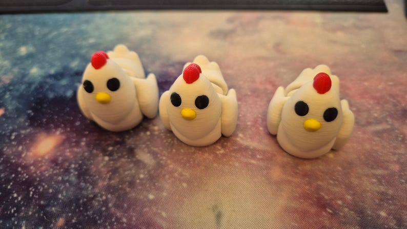 May include: Three white ceramic chicken figurines with red combs and black eyes. The chickens are sitting on a surface with a galaxy pattern.