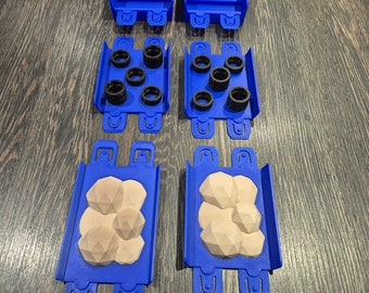 May include: Four blue plastic molds with different shapes. The top two molds are empty. The middle two molds contain black rubber rings. The bottom two molds contain beige, textured, geometric shapes.