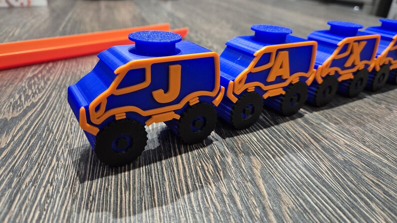May include: A line of five blue toy trucks with orange accents. Each truck has a letter on the side, spelling out the word "JAXON".