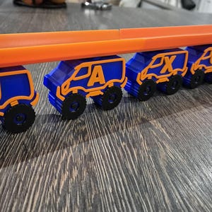 May include: A toy truck train with blue and orange cars. Each car has a letter on it, spelling out the name "JAXXON".