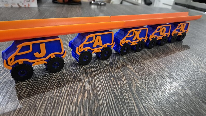 May include: A toy truck train with blue and orange cars. Each car has a letter on it, spelling out the name "JAXXON".