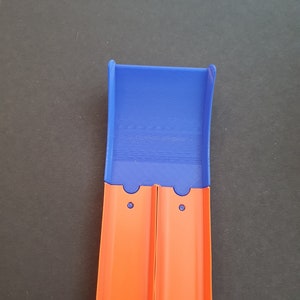 May include: A blue plastic track piece for a toy car race track. The track piece is designed to connect to other track pieces. The track piece is orange and has two holes on the side.