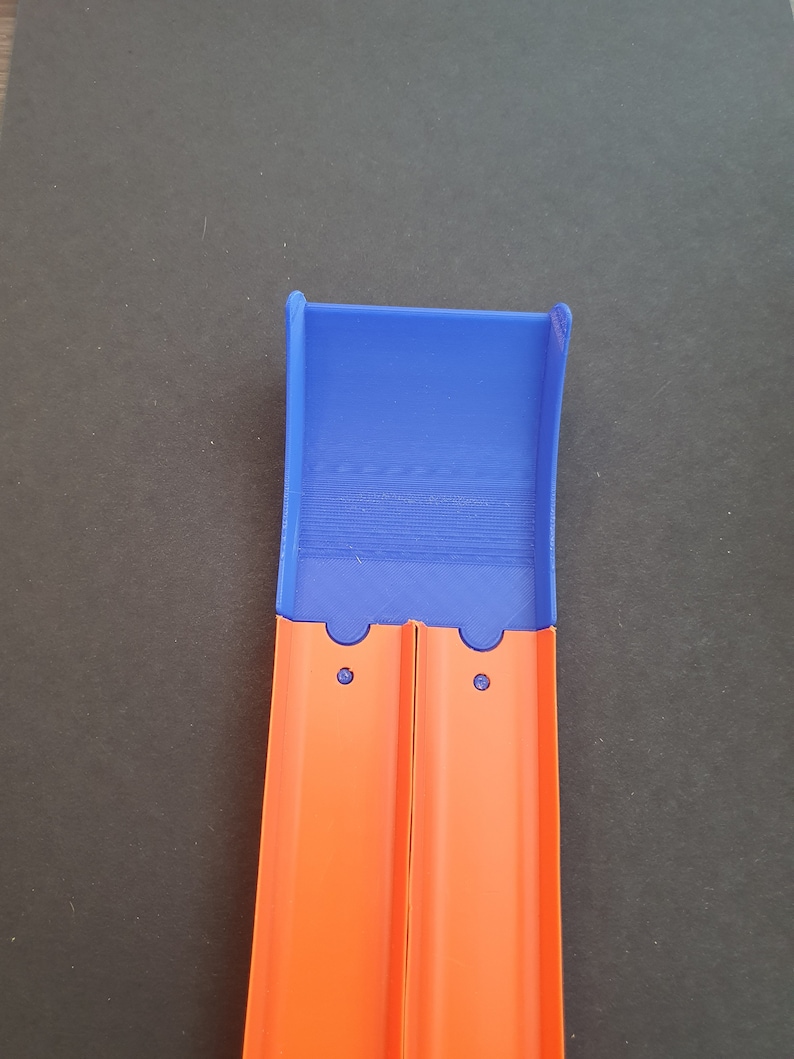 May include: A blue plastic track piece for a toy car race track. The track piece is designed to connect to other track pieces. The track piece is orange and has two holes on the side.