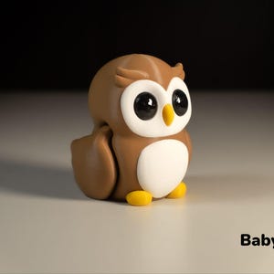 May include: A brown and white owl figurine with large black eyes. The owl is sitting on a white surface. Baby Owl.